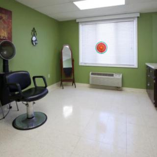 An empty hair salon room with a styling chair and a mirror against green walls.