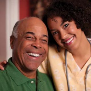 A young woman and an elderly man smiling together indoors.