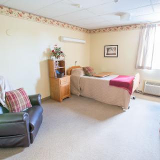 A cozy hospital room featuring a single bed, a chair, and soft decor.