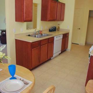 A kitchen with wooden cabinets, a sink, and a dishwasher, adjacent to a small dining area with table settings.
