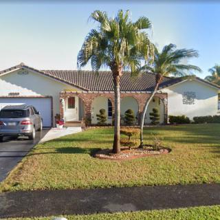 A suburban house with a well-maintained yard and palm trees in front.