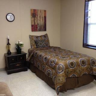 A neatly arranged bedroom featuring a single bed with patterned bedding, a nightstand with decor items, and a window providing natural light.