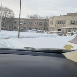 A view from inside a vehicle showing a snowy landscape in front of a school building.