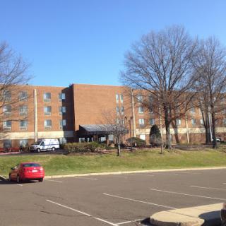 A view of a brick hotel building on a clear day, with trees in the background and cars parked in the lot.