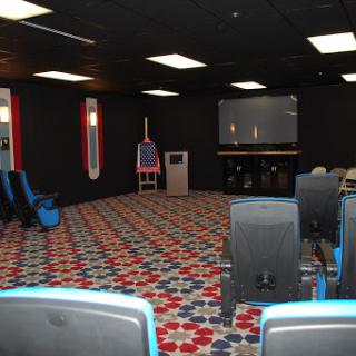 An empty room designed for presentations or gatherings, featuring a projector screen and patterned carpet.