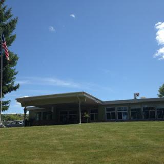 A modern building set against a clear blue sky, featuring a flag and well-manicured grass.