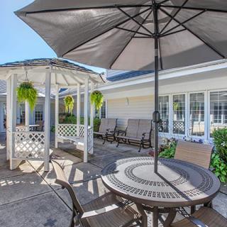 A cozy outdoor patio area with a table, chairs, umbrella, and a gazebo surrounded by plants.