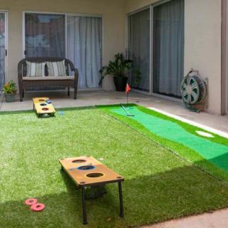 A backyard with a lawn set up for cornhole, featuring outdoor furniture and a patio area.
