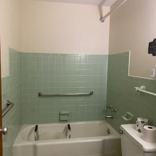 A clean and functional bathroom featuring a bathtub with green tile walls and safety handrails.