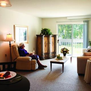 A cozy living room with a person sitting in an armchair near a large window.