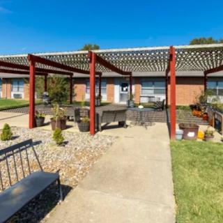 A sunny outdoor garden area featuring a pergola, benches, and a stone pathway.