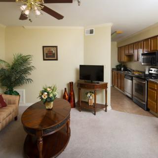A cozy living room with a sofa, coffee table, and television, leading into an open kitchen with modern appliances.