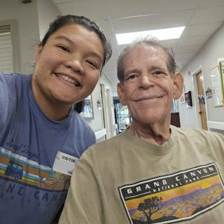 A cheerful selfie taken in a hospital setting, showcasing the bond between a caregiver and an elderly man.