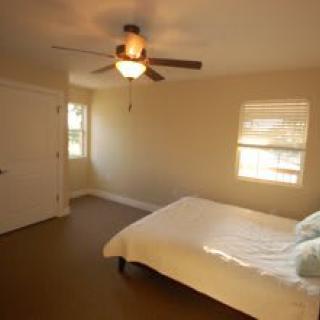 A minimalist bedroom with a ceiling fan, bed, and ample natural light.