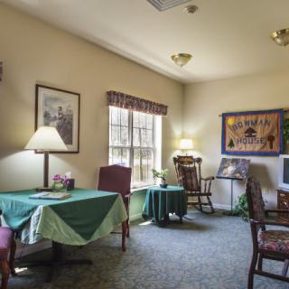 A cozy living room with chairs and tables, decorated with lamps and artwork.