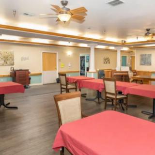 A spacious dining room with red tablecloths, wooden chairs, and ceiling fans.