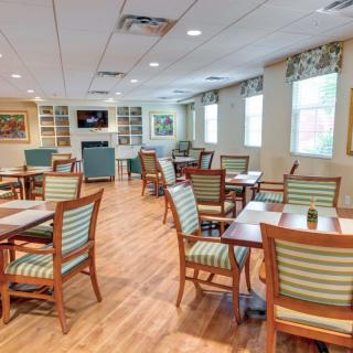 An inviting dining area with wooden floors, multiple tables and chairs, and natural light streaming through the windows.