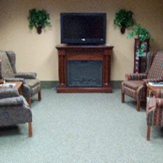 A cozy living room with armchairs arranged around a TV and fireplace, complemented by potted plants.
