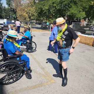 A vibrant outdoor gathering featuring attendees in wheelchairs wearing leis and hats, enjoying a sunny day.