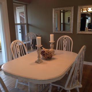 A cozy dining room with a white table and chairs, decorated with candles and a floral centerpiece.