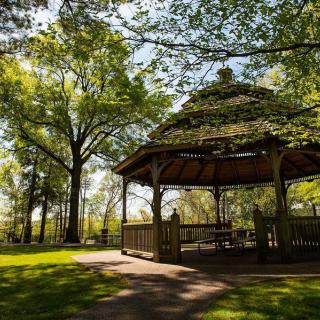 A serene park setting with a wooden gazebo surrounded by lush green trees.