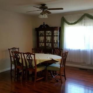 A dining room with a wooden table and chairs, glass cabinet, and a window with curtains.