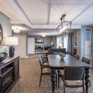 A modern dining room featuring a long wooden table with upholstered chairs, decorative mirrors, and contemporary lighting fixtures.