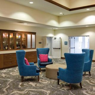 A welcoming lobby area with comfortable blue chairs and a round table, enhanced by soft lighting and a patterned carpet.