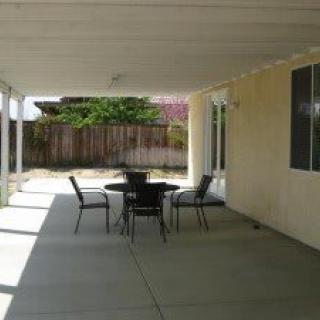 A covered patio area with a table and chairs, overlooking a backyard.
