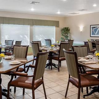 An empty dining room with neatly arranged tables and chairs, featuring large windows and bright lighting.
