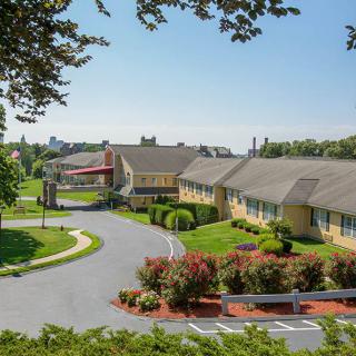 A scenic view of a hotel building surrounded by landscaped greenery and parking area under a clear blue sky.