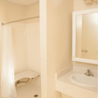 A beige bathroom with a shower, sink, and mirror.