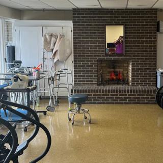 A basement room featuring a brick fireplace, various chairs, and tables.