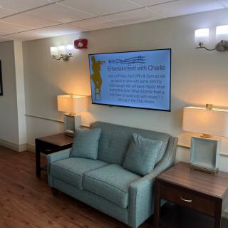 A cozy lobby area with a couch, lamps, and a large television displaying information.