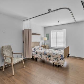 A minimalist bedroom with a single bed, chair, and wooden flooring.