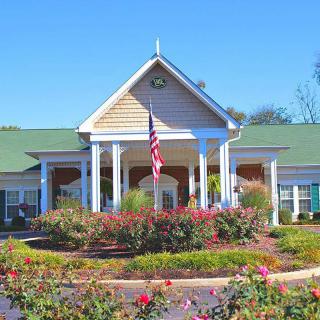 A large house with a green roof and white columns, surrounded by well-maintained gardens and an American flag in front.