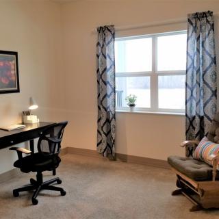 A cozy home office with a desk, chair, and a window with patterned curtains.