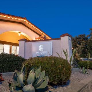 A well-lit hotel exterior with landscaped bushes and a prominent sign, captured at night.