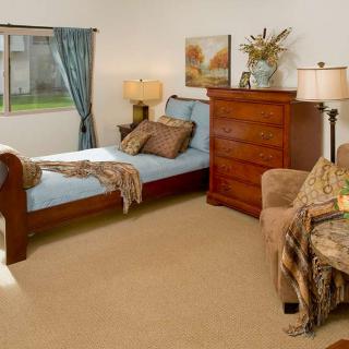 A cozy bedroom featuring a single bed, wooden dresser, and an armchair with decorations.