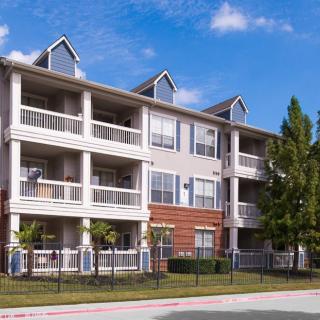 A three-story apartment building with balconies under a clear blue sky.