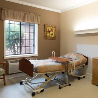 A patient room in a hospital, featuring a bed, chair, and window.