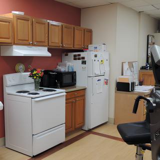 An office kitchen area with a stove, refrigerator, microwave, and wooden cabinets.