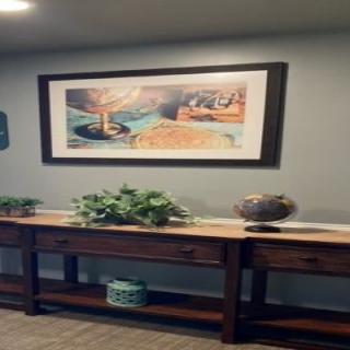 A hallway with a painting above a wooden table, decorated with plants and a vase.
