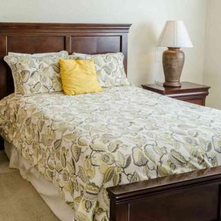 A cozy bedroom with a wooden bedframe, floral bedding, and a nightstand with a lamp.