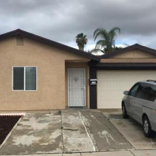 A residential house with a driveway and a car parked in front under a cloudy sky.