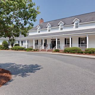A colonial-style building with a white facade, featuring a porch and surrounding landscaping.