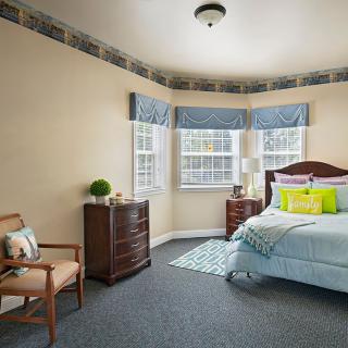 A cozy bedroom with a bed, chair, and large windows providing natural light.