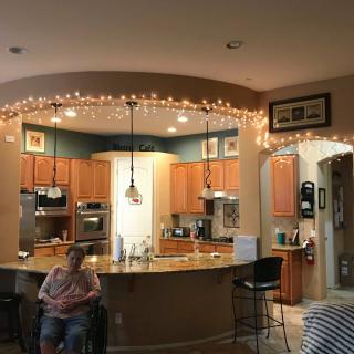 A modern kitchen with wooden cabinets, decorated with string lights, featuring a counter and stools.