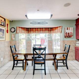 A cozy dining area with a wooden table and chairs, brightened by natural light from a large window with patterned curtains.