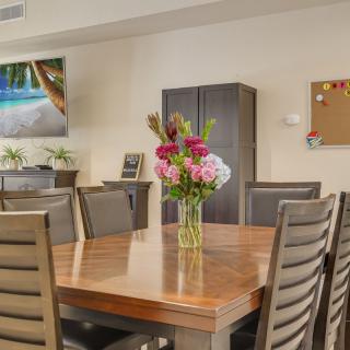 A dining room with a wooden table, surrounded by chairs, and a vase of colorful flowers as the centerpiece.